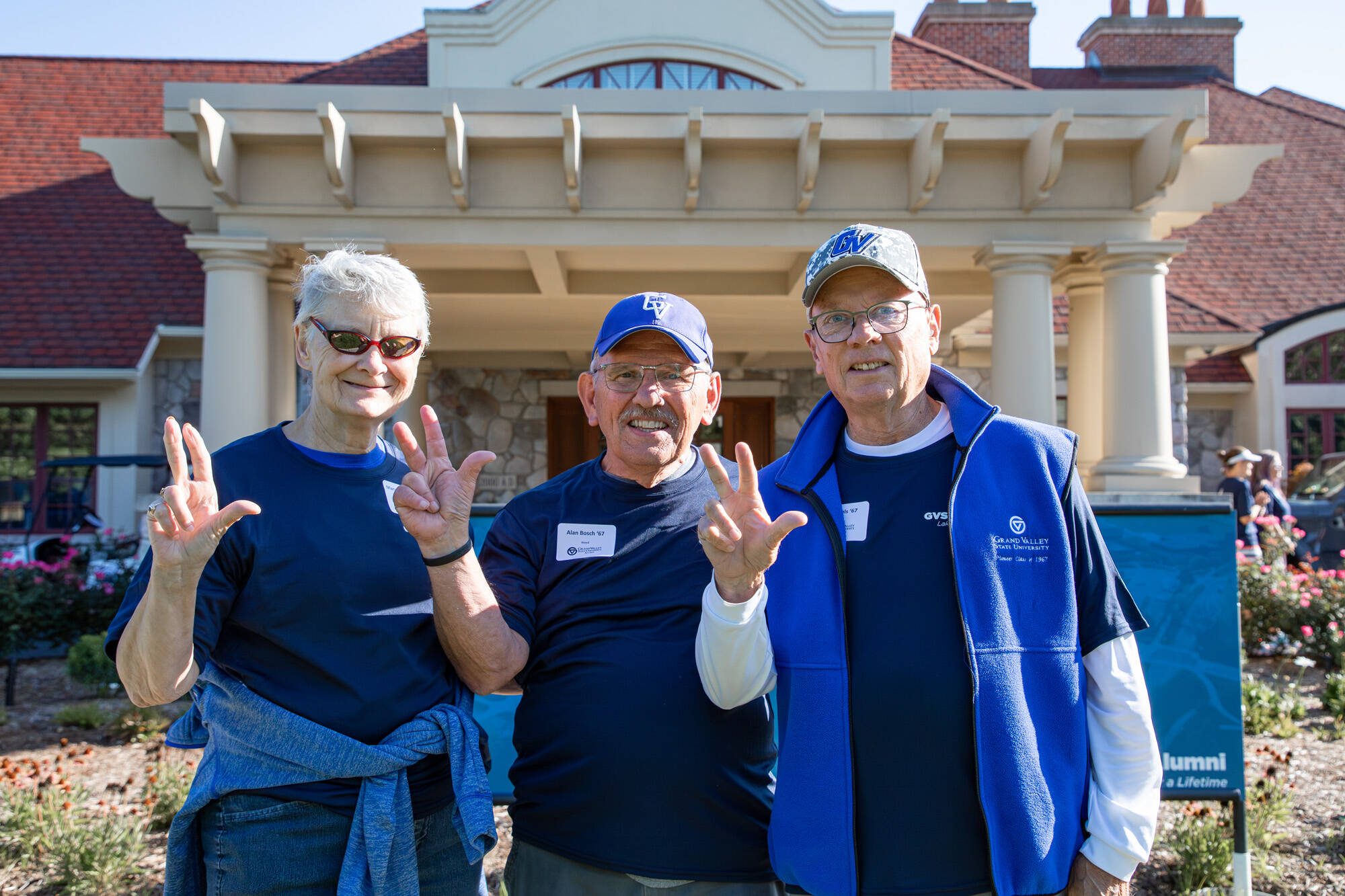 Three older alumni in move-in-day volunteer t-shirts